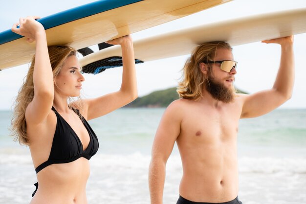 Giovane uomo e donna che tengono le tavole da surf sulla testa e camminano nel mare per fare surf