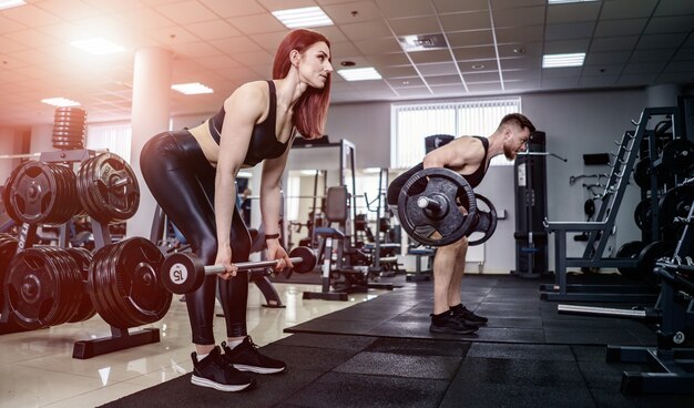 - giovane uomo e donna con bilanciere flettendo i muscoli e facendo squat pressa spalle in palestra. Avvicinamento. Concetto di vita sana.