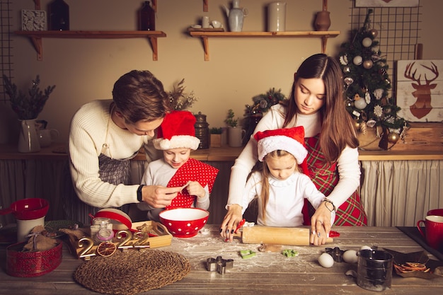 Giovane uomo e ragazza insegnano ai bambini come cucinare i biscotti in cucina decorazioni natalizie tradizioni familiari cibo natalizio vigilia delle vacanze master class