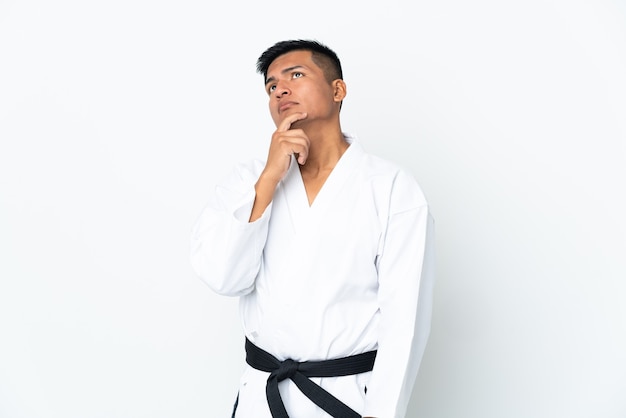 Giovane uomo ecuadoriano che fa karate isolato sulla parete bianca che ha dubbi