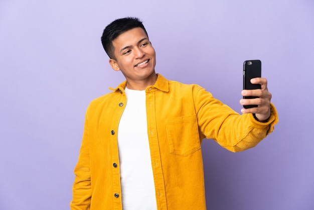 Giovane uomo ecuadoriano isolato sulla parete viola facendo un selfie