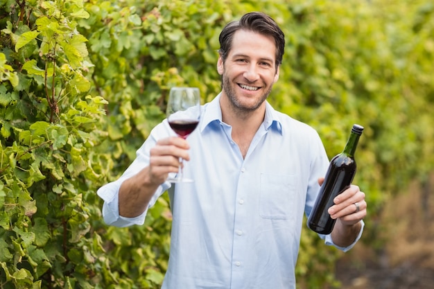 Giovane uomo felice che sorride alla macchina fotografica e che tiene un bicchiere di vino