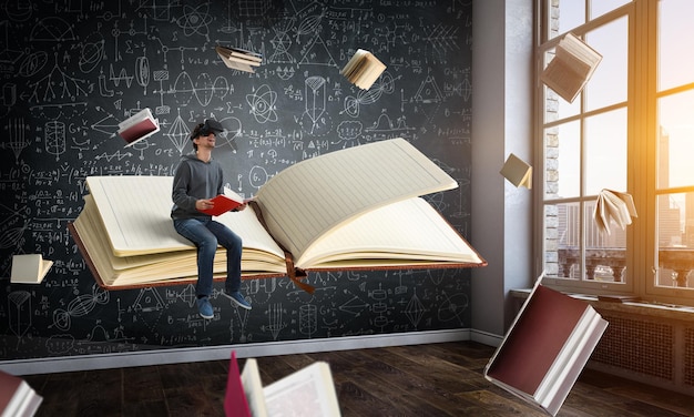 Giovane uomo felice in cuffia VR con libri in una classe. Tecnica mista