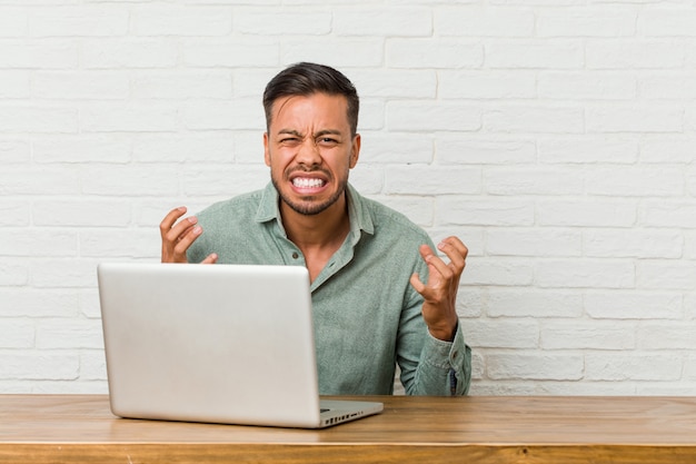 Giovane uomo filippino seduto a lavorare con il suo laptop urlando di rabbia.