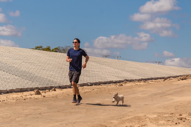 Giovane uomo fitness jogging con il suo cucciolo al suo fianco nella sabbia.