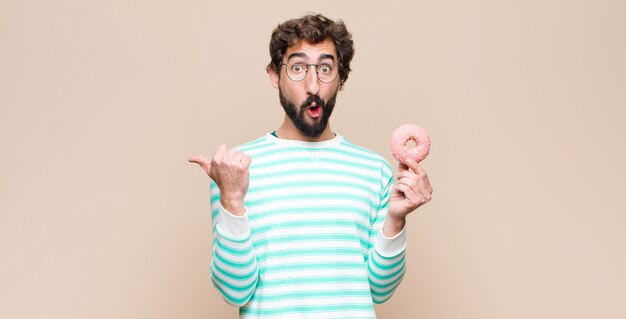 Giovane uomo freddo con una ciambella rosa zucchero contro la parete piatta