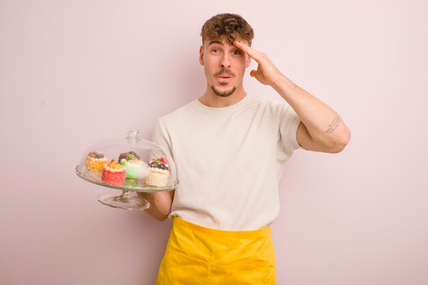 Giovane uomo fresco che sembra felice stupito e sorpreso concetto di torte fatte in casa