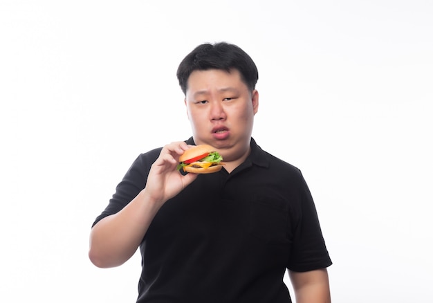 Giovane uomo grasso asiatico in camicia di polo nera che mangia hamburger con il fronte felice