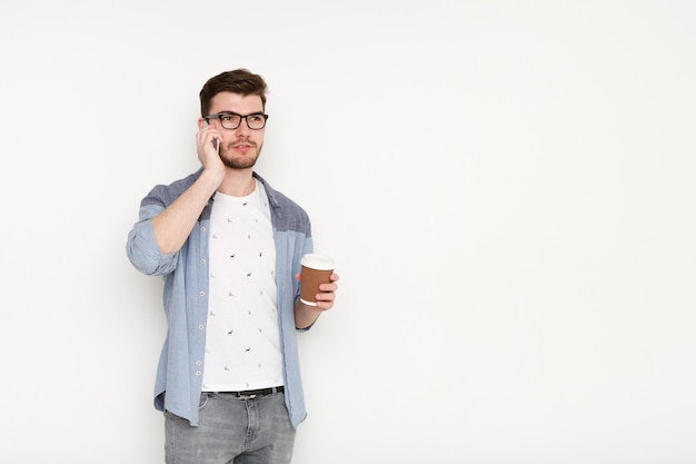 Giovane uomo impegnato a parlare al telefono con una tazza di caffè. Ritratto di ragazzo sicuro, stile di vita moderno, concetto di comunicazione