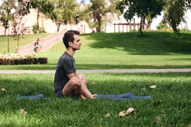 Giovane uomo in abiti sportivi che fa yoga nel parco