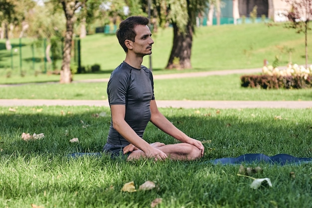 Giovane uomo in abiti sportivi che fa yoga nel parco