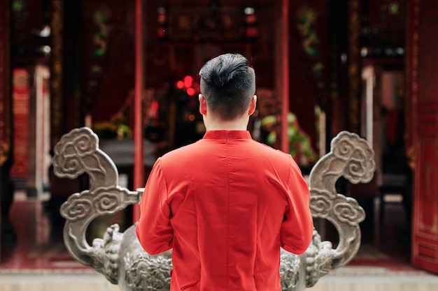 Giovane uomo in camicia rossa che prega all'urna di rame nel tempio, vista dal retro