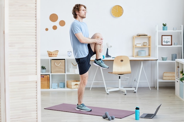 Giovane uomo in piedi sulla stuoia di esercizio e facendo esercizi sportivi in camera a casa