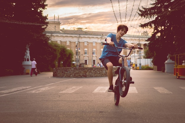 Giovane uomo in sella a una bici bmx su una ruota posteriore posteriore, facendo acrobazie in città