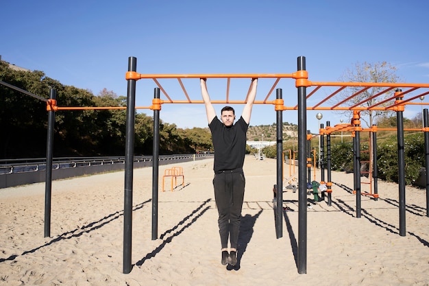 Giovane uomo in un parco con bilancieri facendo pull up, ginnastica ritmica. Esercizio all'aperto con bilanciere, fitness, sport, allenamento e concetto di stile di vita.