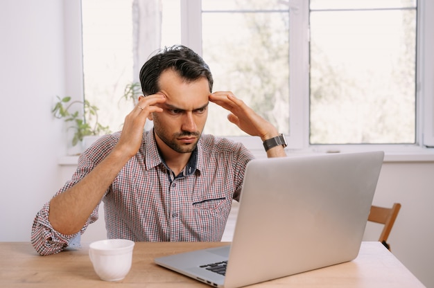 Giovane uomo in una camicia che lavora su un computer portatile a casa