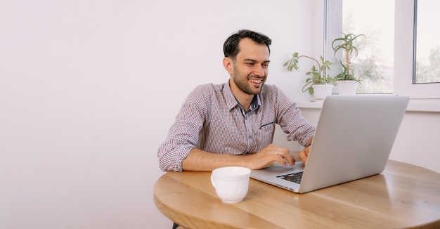 Giovane uomo in una camicia che lavora su un computer portatile a casa