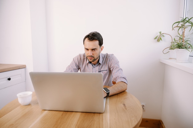 Giovane uomo in una camicia che lavora su un computer portatile a casa