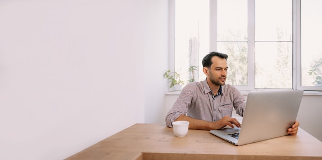 Giovane uomo in una camicia che lavora su un computer portatile a casa