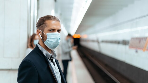 giovane uomo in una maschera protettiva in piedi in una stazione della metropolitana