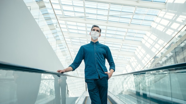 Giovane uomo in una maschera protettiva in piedi sui gradini della scala mobile.