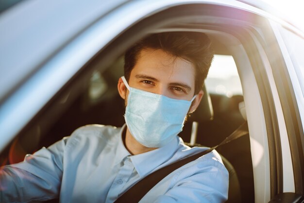 Giovane uomo in una maschera protettiva seduto in macchina