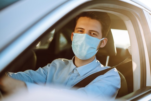 Giovane uomo in una maschera protettiva seduto in macchina