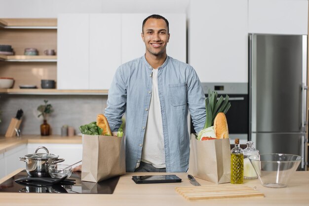 Giovane uomo indiano attraente positivo che prepara cibo sano per insalata da verdure biologiche fresche