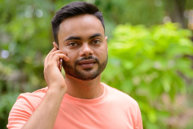 Giovane uomo indiano barbuto bello che parla al telefono al parco