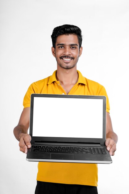 Giovane uomo indiano che mostra lo schermo del computer portatile con lo spazio della copia su fondo bianco.