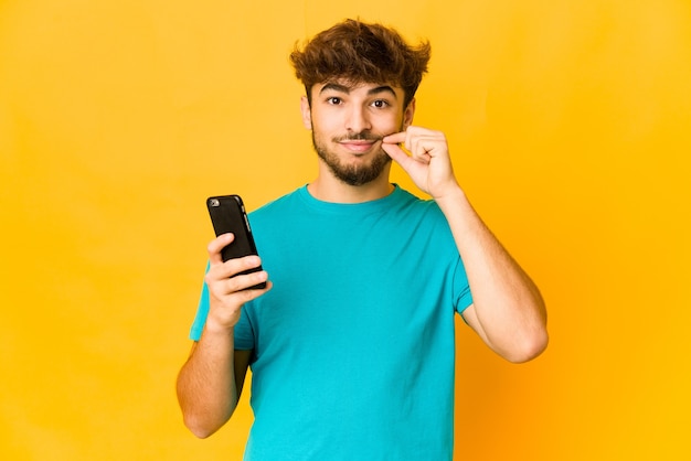 Giovane uomo indiano che tiene un telefono con le dita sulle labbra mantenendo un segreto.