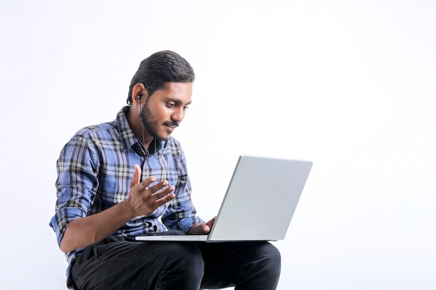Giovane uomo indiano che utilizza computer portatile sopra fondo bianco.