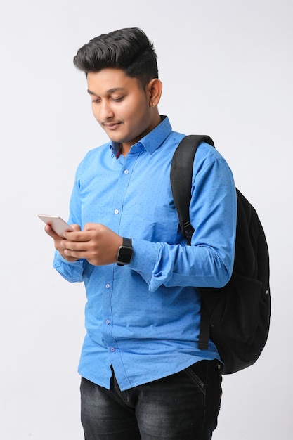 Giovane uomo indiano che utilizza smartphone e dà espressione su sfondo bianco.