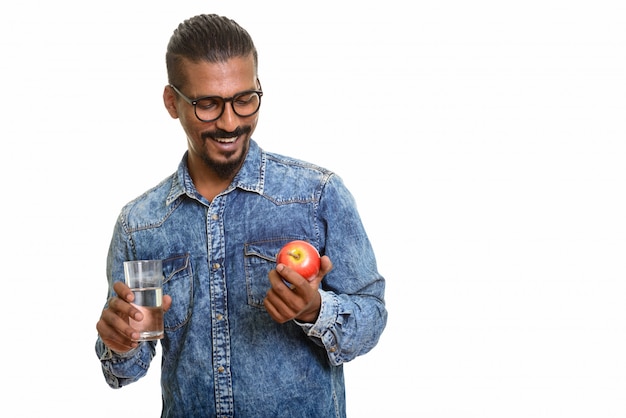 Giovane uomo indiano felice che tiene mela rossa e bicchiere d'acqua isolati