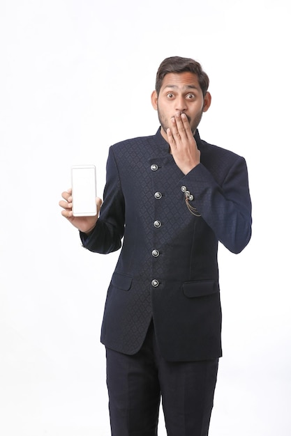 Giovane uomo indiano nella tradizione indossa e mostra lo schermo dello smartphone su sfondo bianco.