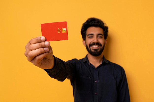 Giovane uomo indiano sorridente che mostra la carta di credito alla macchina fotografica
