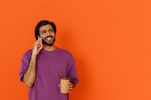 Giovane uomo indiano sorridente in maglietta che beve caffè da asporto