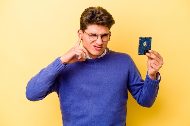 Giovane uomo informatico caucasico isolato su sfondo giallo che copre le orecchie con le mani