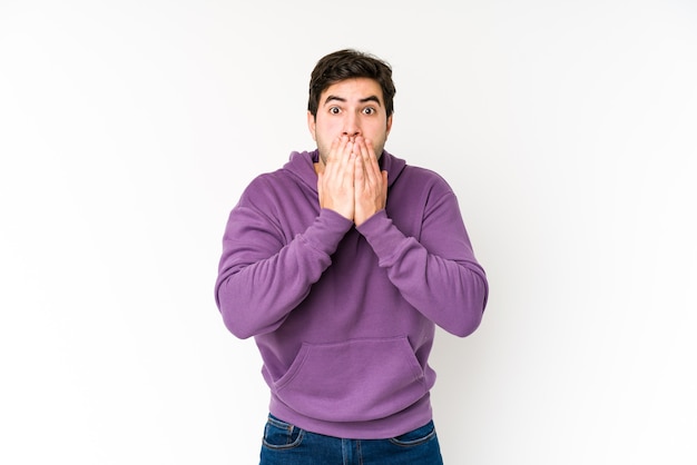 Giovane uomo isolato su sfondo bianco scioccato che copre la bocca con le mani.