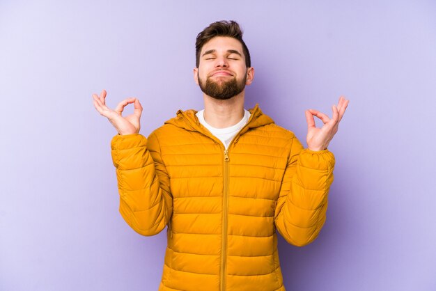 Giovane uomo isolato su sfondo viola si rilassa dopo una dura giornata di lavoro, lei sta eseguendo yoga.