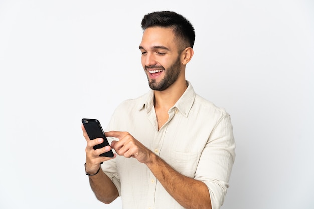 Giovane uomo isolato sul muro bianco, inviando un messaggio o e-mail con il cellulare