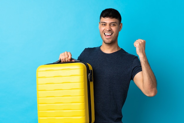 Giovane uomo isolato sull'azzurro in vacanza con la valigia da viaggio