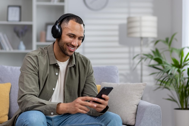 Giovane uomo ispanico a casa seduto sul divano che riposa uomo con le cuffie che ascolta la radio musicale online