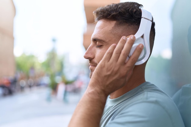 Giovane uomo ispanico che ascolta la musica in piedi in strada