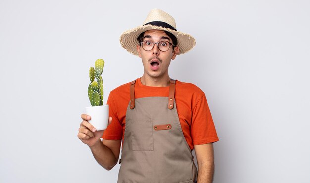 Giovane uomo ispanico che sembra molto scioccato o sorpreso. giardiniere con il concetto di cactus