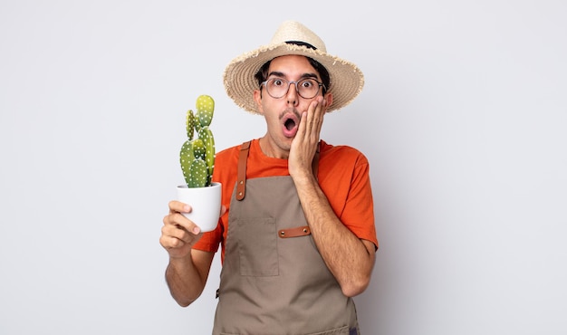 Giovane uomo ispanico che si sente scioccato e spaventato. giardiniere con il concetto di cactus