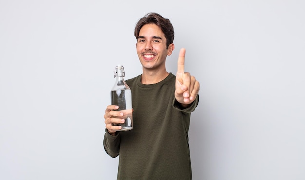 Giovane uomo ispanico che sorride con orgoglio e sicurezza facendo il concetto di bottiglia d'acqua numero uno
