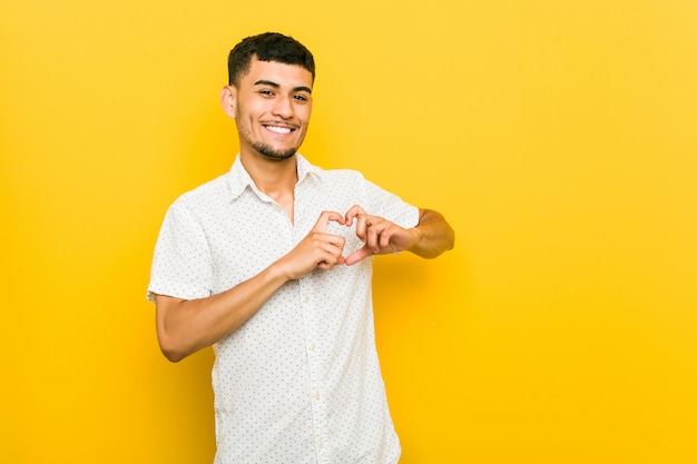 Giovane uomo ispanico che sorride e che mostra una forma del cuore con le mani.