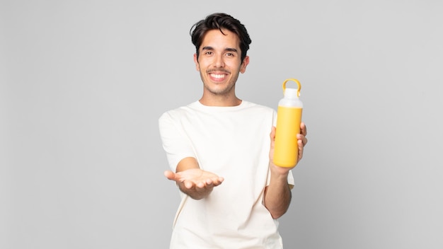 Giovane uomo ispanico che sorride felicemente con amichevole e offrendo e mostrando un concetto con un thermos di caffè