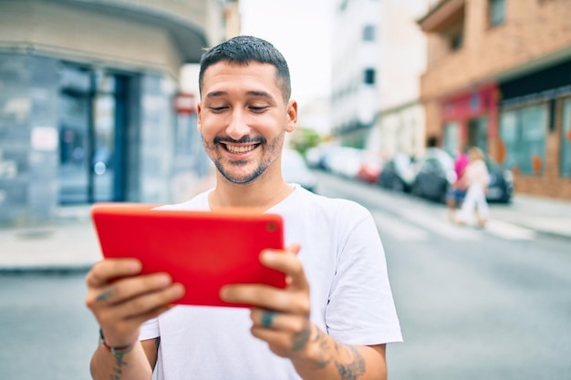 Giovane uomo ispanico che utilizza il touchpad che cammina per strada della città.